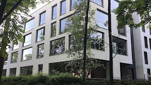 Moderni rakennus, jossa on useita kerroksia ja suuret ikkunat, ja sen ympärillä on hyvin hoidettua viheraluetta.