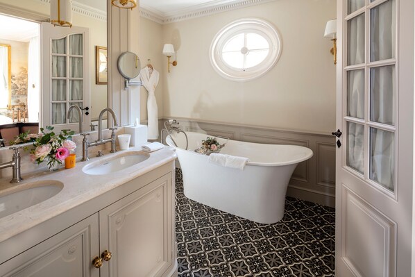 A bathroom with a freestanding bathtub, two sinks, a large mirror, and a window with a view. - Villa Saint-Ange Hôtel & Spa (Aix-en-Provence)
