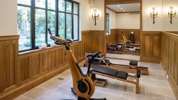 Academia com equipamentos de ginástica, janelas amplas e painéis de madeira.