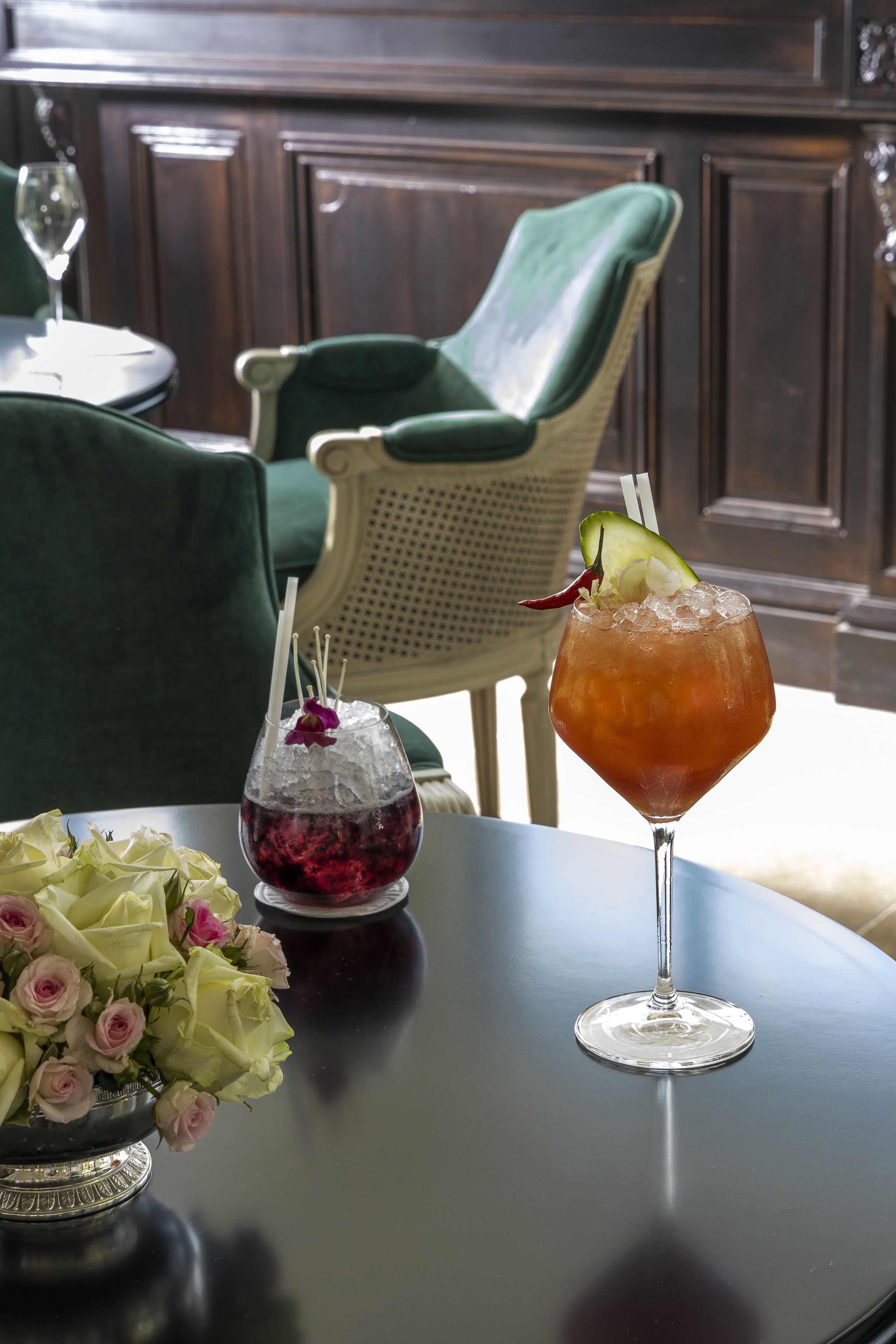 A table with a cocktail glass, a bowl of fruit, and a vase of flowers.