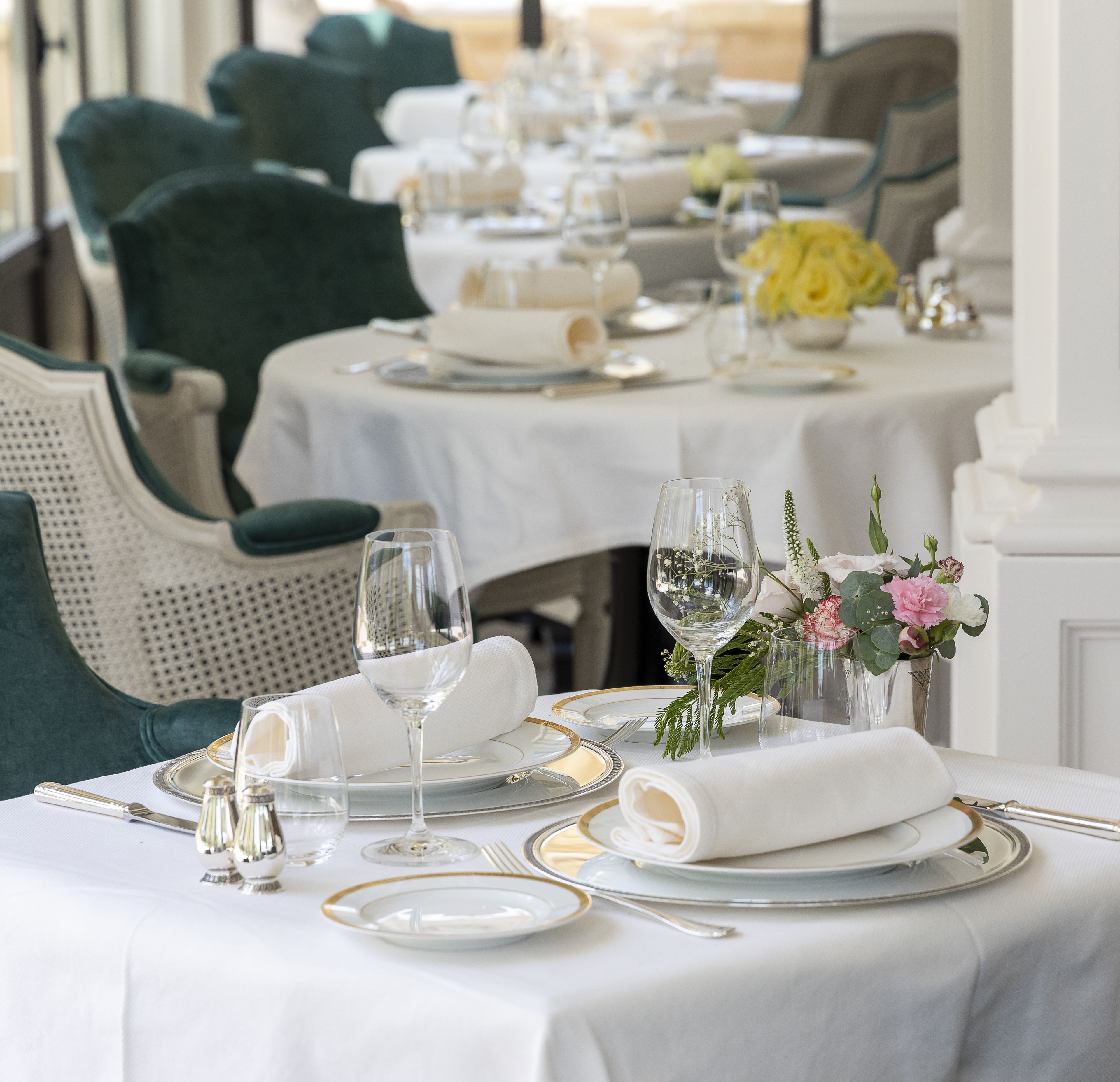 Une table à manger dressée avec des nappes blanches, des assiettes à bord doré et des couverts en argent.