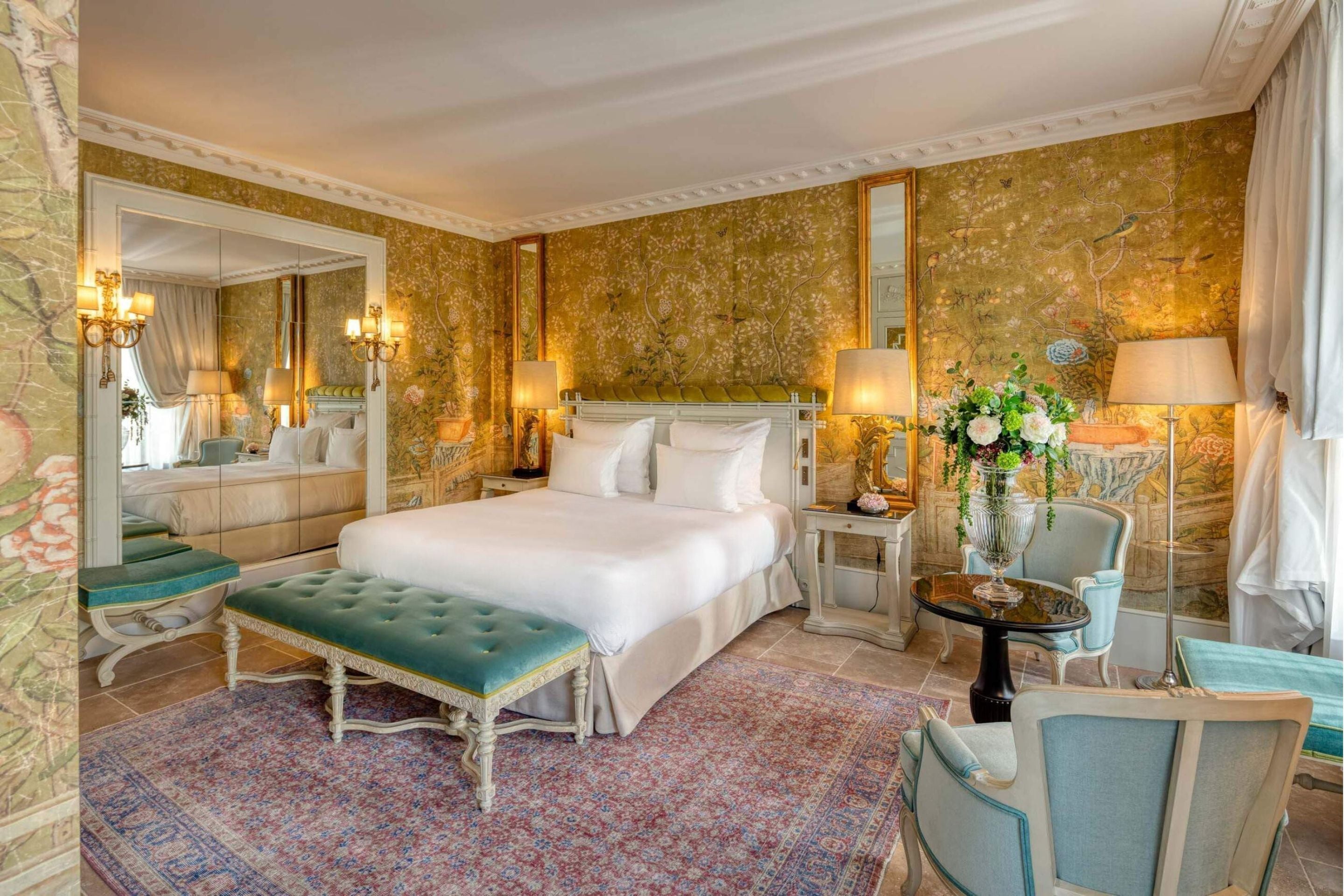 A spacious bedroom with a large bed, a sitting area with a table and chairs, and a decorative mirror.