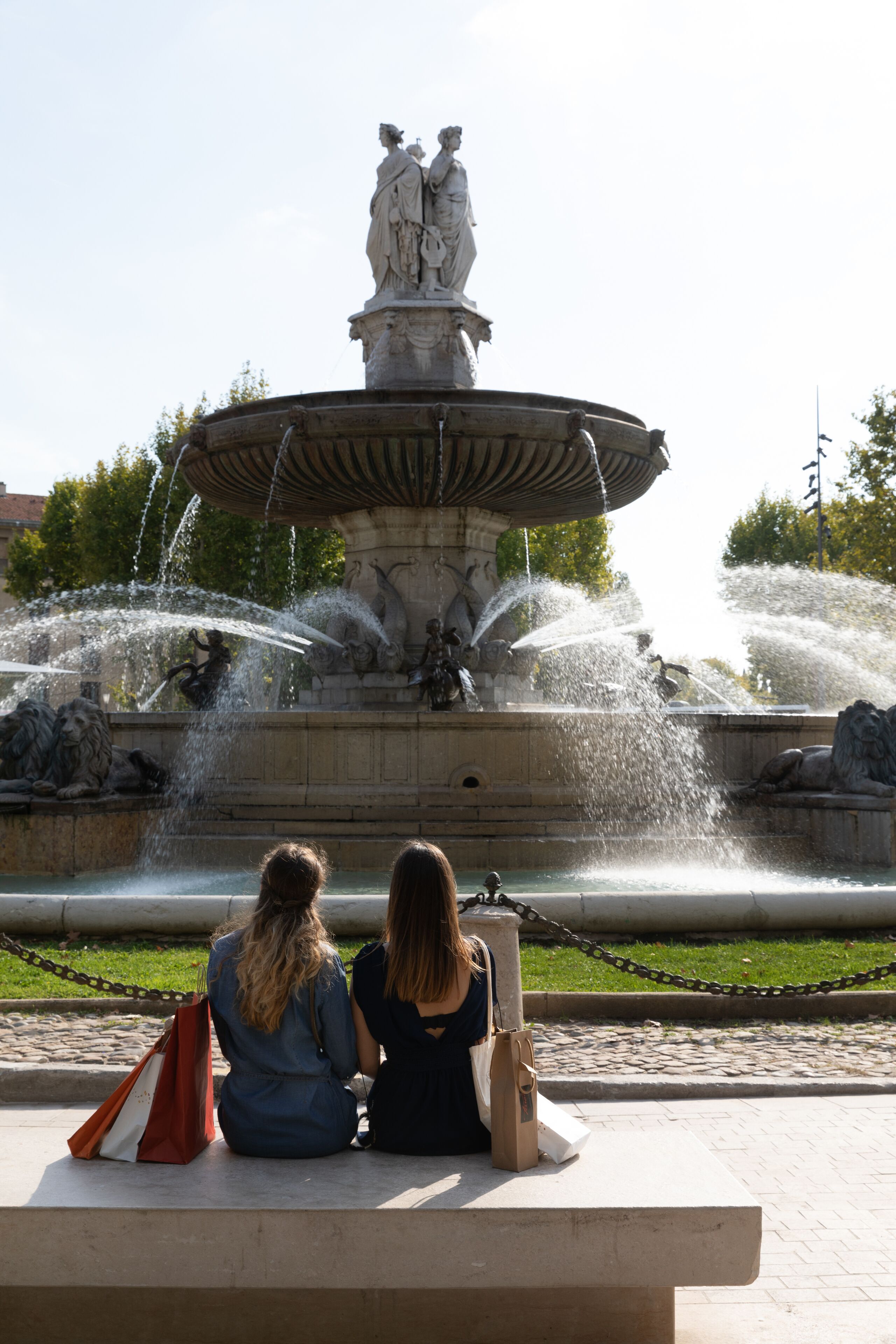 A fountain with statues and water jets, surrounded by a paved area with benches.