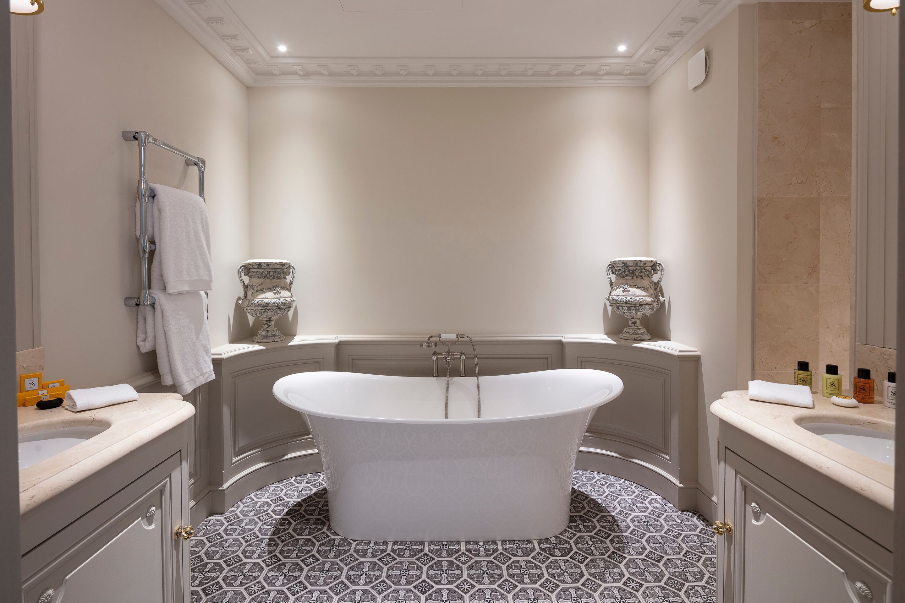 Un baño moderno con una bañera independiente, dos lavamanos y baldosas de suelo estampadas.