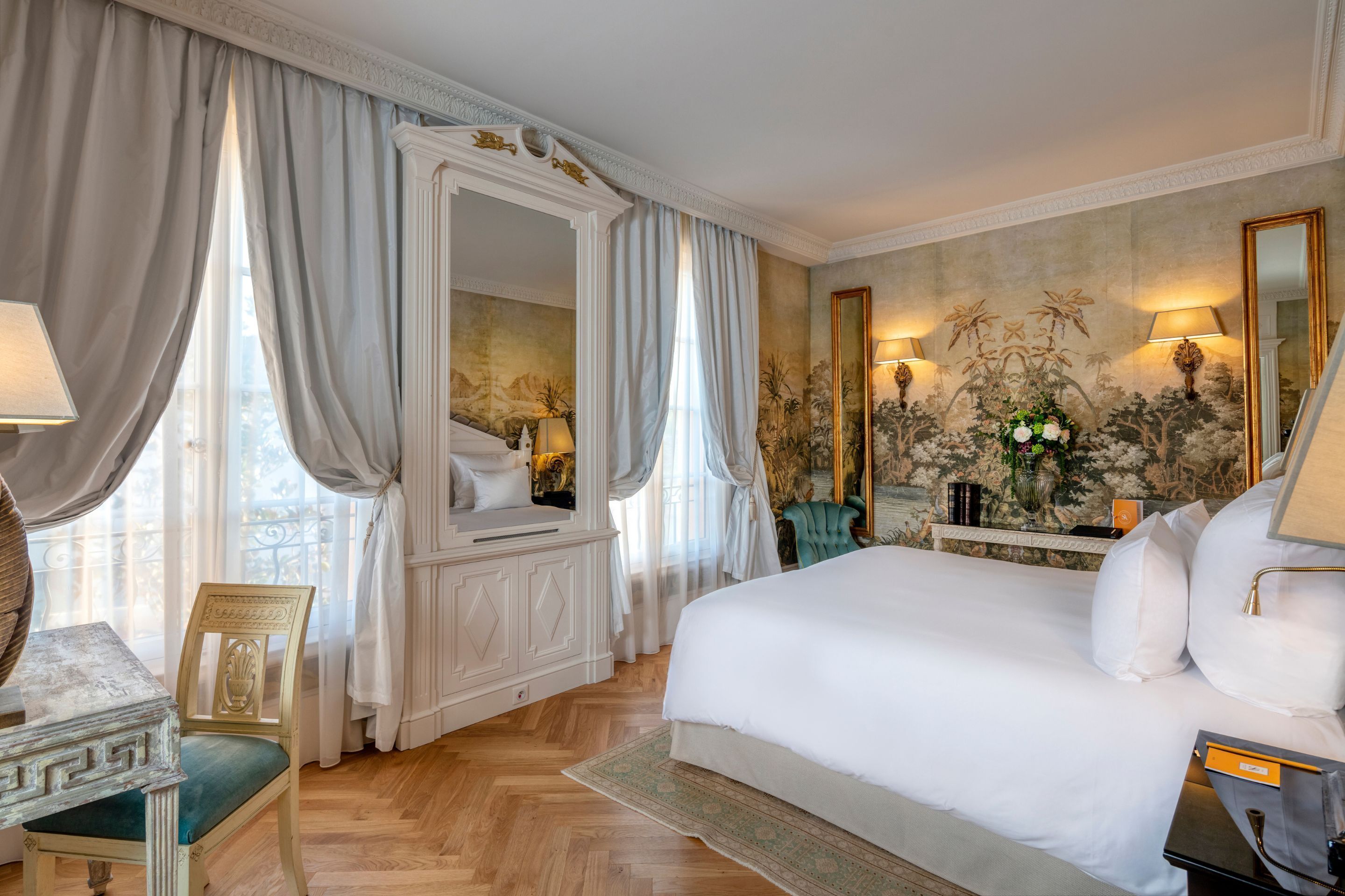A spacious bedroom with a large bed, a vanity with a mirror, and a seating area with a chair.
