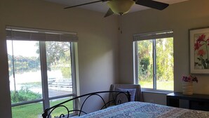 A bedroom with a bed, a ceiling fan, and large windows with a view of a lake and greenery. - Lakefront VERY PRIVATE Guest House with Gorgeous Lake Views!  2-Bed, 2-Bath (Brandon)