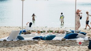 Ein Strandbild mit Sonnenschirmen, Liegestühlen und einem für das Essen gedeckten Tisch.