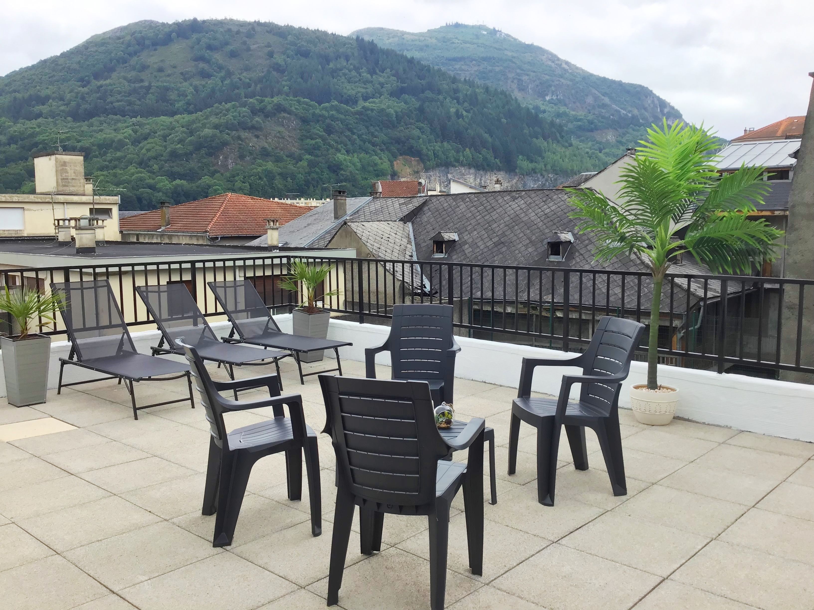 A rooftop terrace with black plastic chairs and tables, surrounded by a black metal railing.
