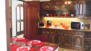 Une cuisine avec des meubles de rangement en bois, un four à micro-ondes et une table à manger agrémentée de sets de table et d’assiettes rouges.