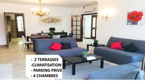 Un salon moderne avec un canapé gris, une table à manger et un lustre. Il y a deux terrasses, un espace de stationnement privé et quatre chambres.
