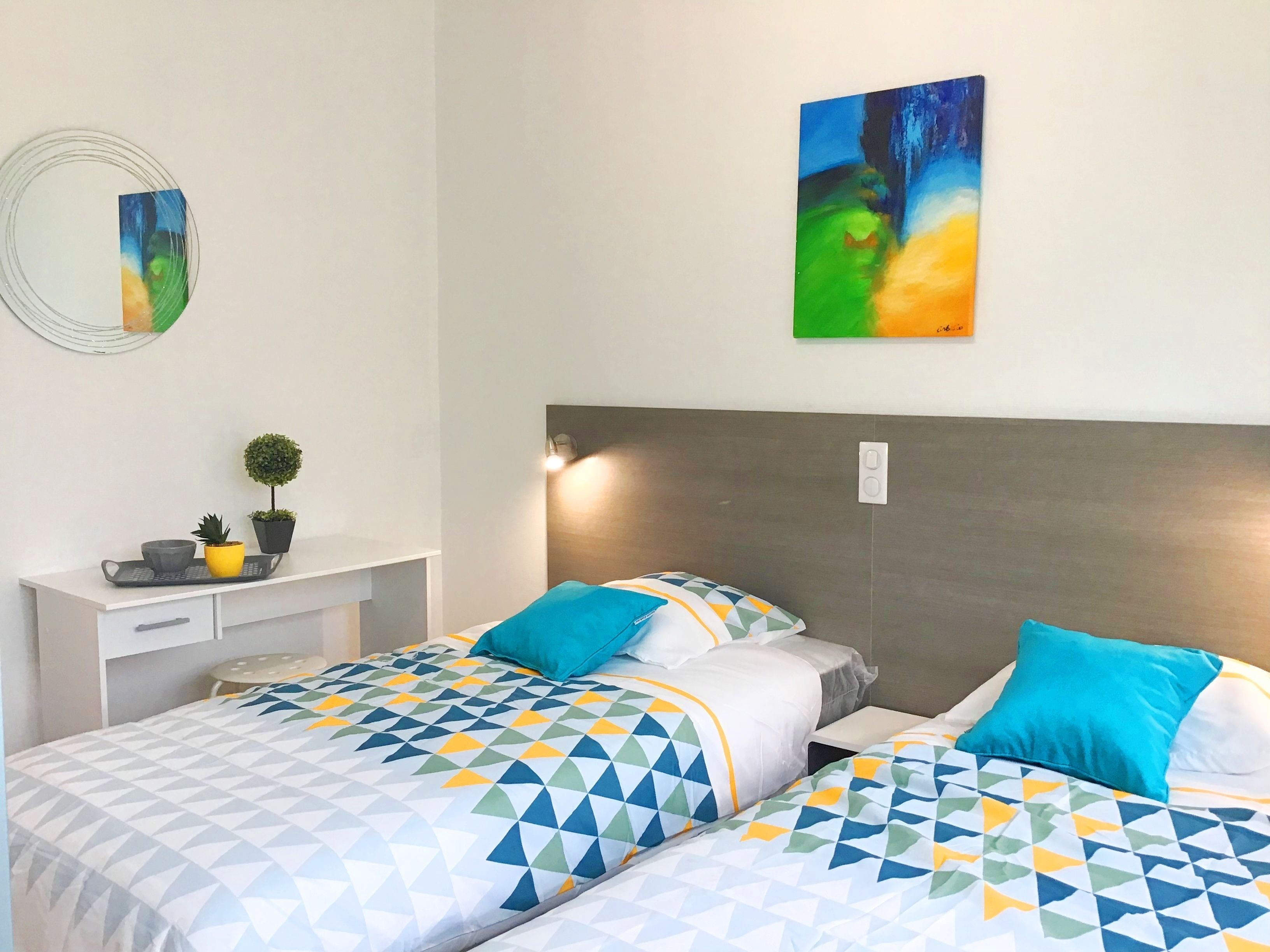 Ein Hotelzimmer mit zwei Betten, einem Schreibtisch und einem an der Wand hängenden Gemälde.