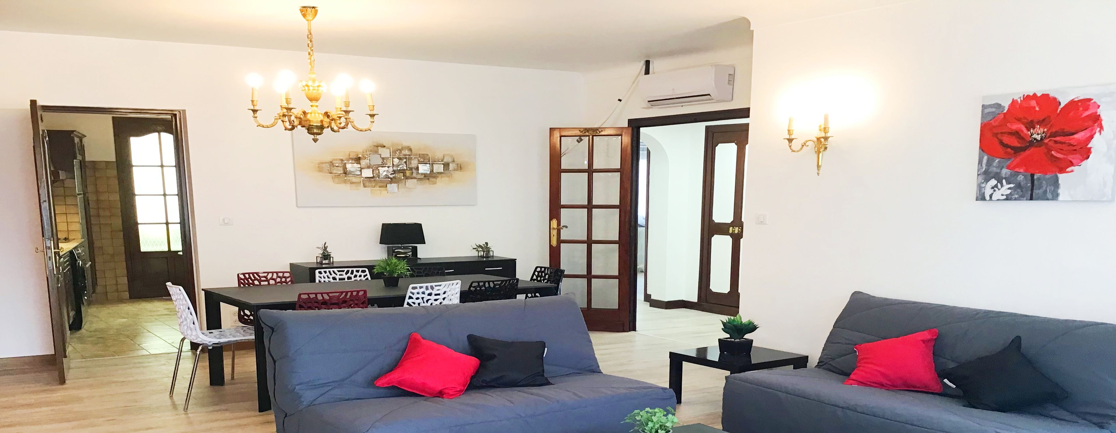 A modern living room with a grey sofa, a dining table, and a chandelier. There are two terraces, a private parking area, and four bedrooms.