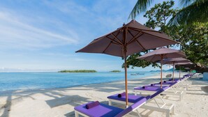A beach with white lounge chairs and purple cushions, arranged in rows under large umbrellas. - La Vida Samui (Koh Samui)