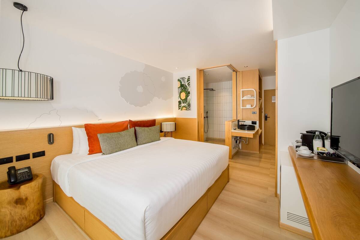A modern hotel room with a large bed, a bedside telephone, a wooden headboard, a wall-mounted lamp, and a television on a wooden stand.