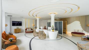 A modern lobby with a reception desk, seating areas, and a large flat-screen TV.