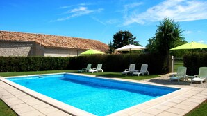 Una piscina rectangular con un borde de baldosas, rodeada de sillas de descanso blancas y sombrillas verdes.