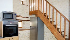 Una cocina con horno Bosch, microondas y refrigerador. A la derecha, una escalera de madera.
