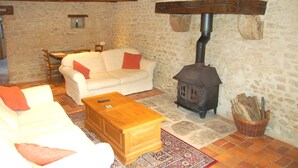 Una sala de estar acogedora con una pared de piedra, un sofá blanco, una mesa de centro de madera y un estufa de leña.