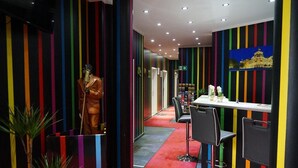 Un pasillo de colores vivos con paredes a rayas, un maniquí con traje y un área de comedor con sillas y una mesa.