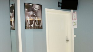Una habitación con una puerta blanca, un cuadro enmarcado de una máquina de café y un televisor montado en la pared.