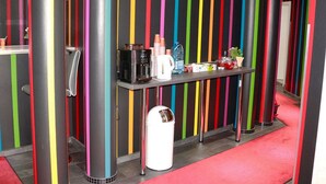 Un baño moderno con rayas verticales de colores en las paredes, una cafetera y artículos de aseo en un mostrador.