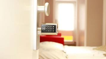 A hotel room with a bed, a red chair, and a door with a keypad lock.
