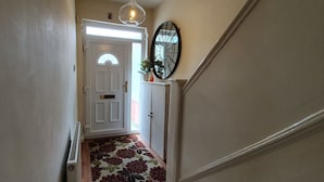 Un couloir avec une porte blanche, un radiateur, une moquette à motifs floraux et un miroir fixé au mur.