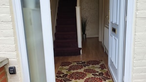 Un couloir avec un escalier recouvert de moquette, une porte blanche et un mur en briques.