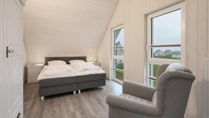 Et soveværelse med en stor seng, en stol og udsigt til huse gennem et vindue.