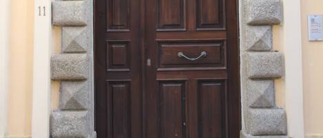 A dark wooden door with a circular handle, flanked by stone pillars with geometric patterns, set within a beige wall with a stone arch above.