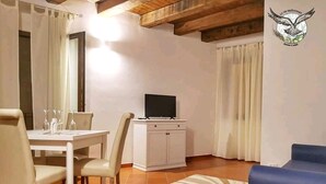 A dining area with a table set for two, a television on a cabinet, and a blue sofa. - Le Vie Mediterranee (Torre di Ruggiero)