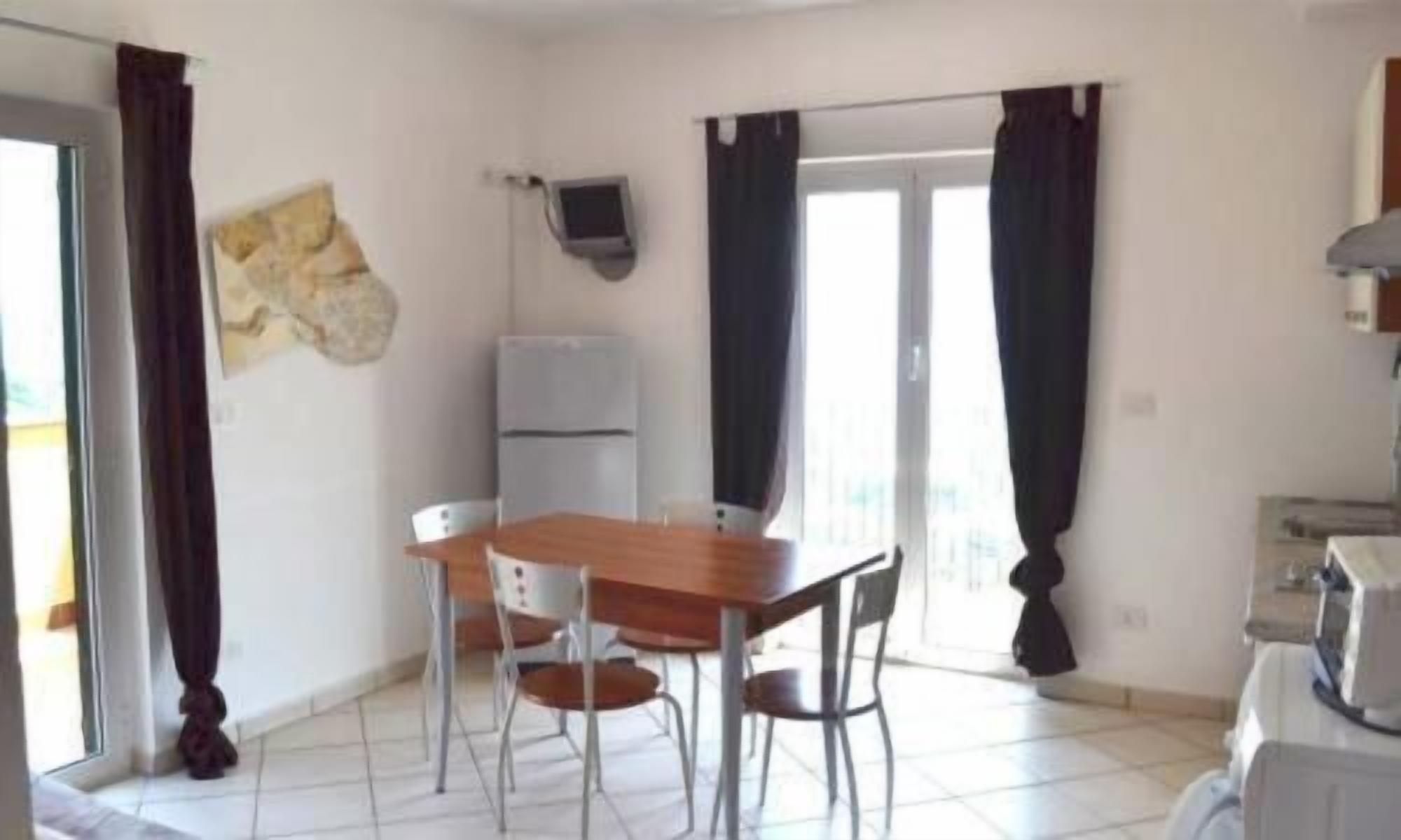 A small, bright room with a wooden table and chairs, a refrigerator, and a TV mounted on the wall.