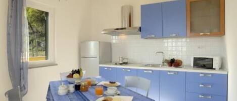 A compact kitchen with blue cabinets, a white countertop, and a dining table set for breakfast.