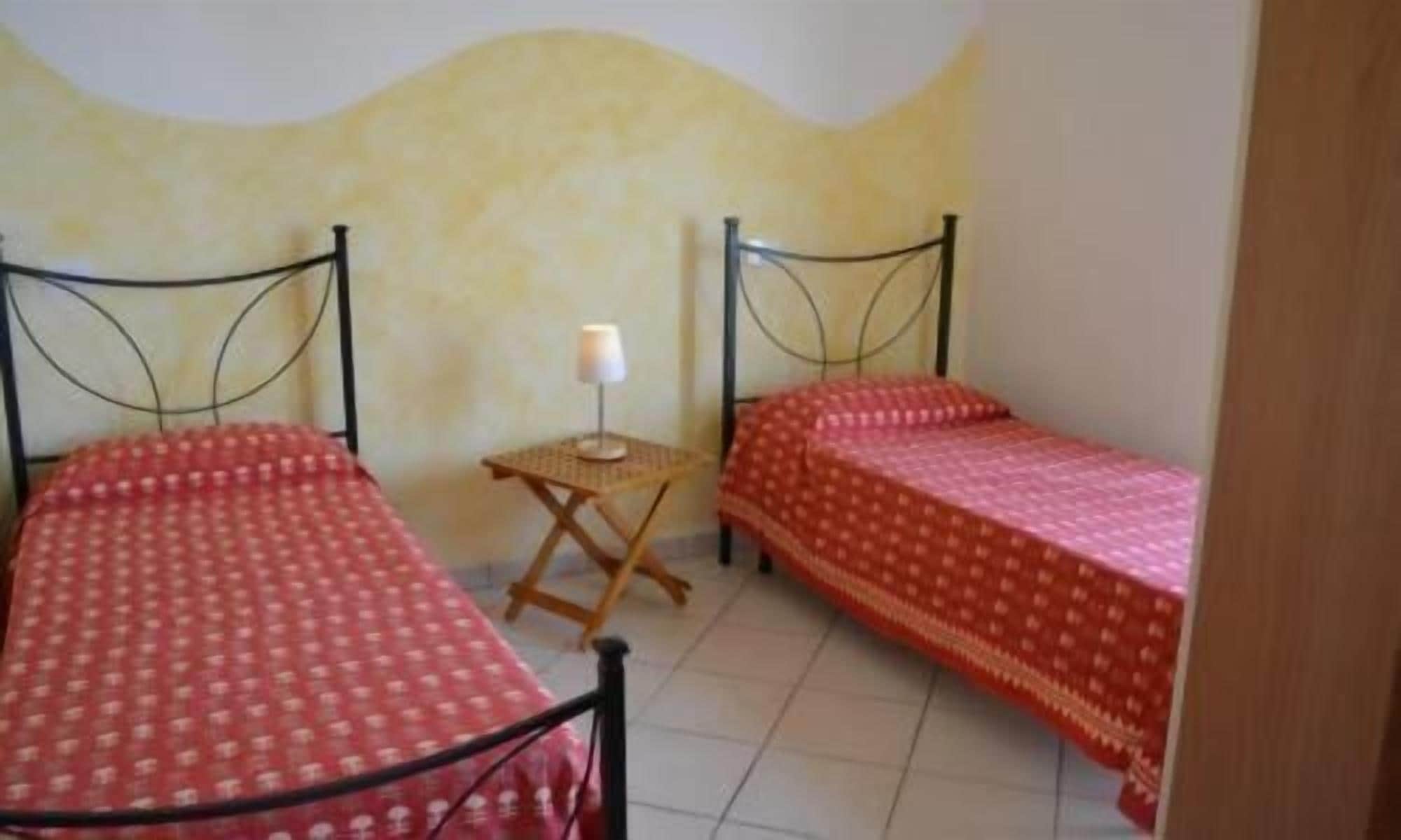 Een kleine kamer met twee eenpersoonsbedden, een tafeltje en een lamp.
