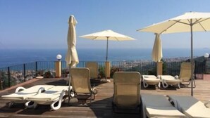 A deck with lounge chairs and umbrellas overlooking a coastal cityscape.