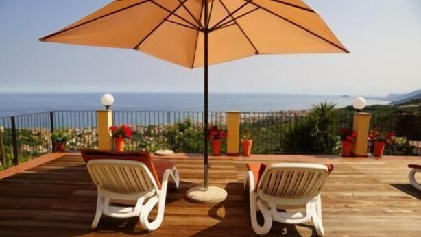 A wooden deck with two white chairs and a large umbrella, overlooking a coastal view.