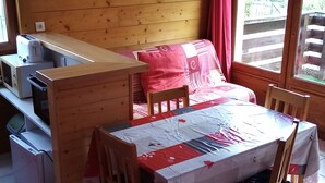 A compact room with a wooden table and chairs, a sofa with a red blanket, and a kitchenette area with a toaster and microwave. - Chalet with superb mountain views, very central. (Saint-Diéry)