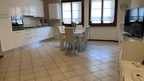 A modern kitchen with white cabinets, a dining table with chairs, and a TV on a stand. - A very large holiday home in Valpolicella, suitable for several families, (Arbizzano-Santa Maria)