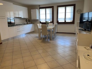 A modern kitchen with white cabinets, a dining table with chairs, and a TV on a stand.