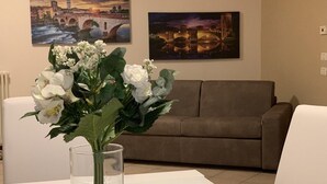 A living room with a brown sofa, a white table, and a vase with white flowers. There are two paintings on the wall depicting cityscapes. - A very large holiday home in Valpolicella, suitable for several families, (Arbizzano-Santa Maria)