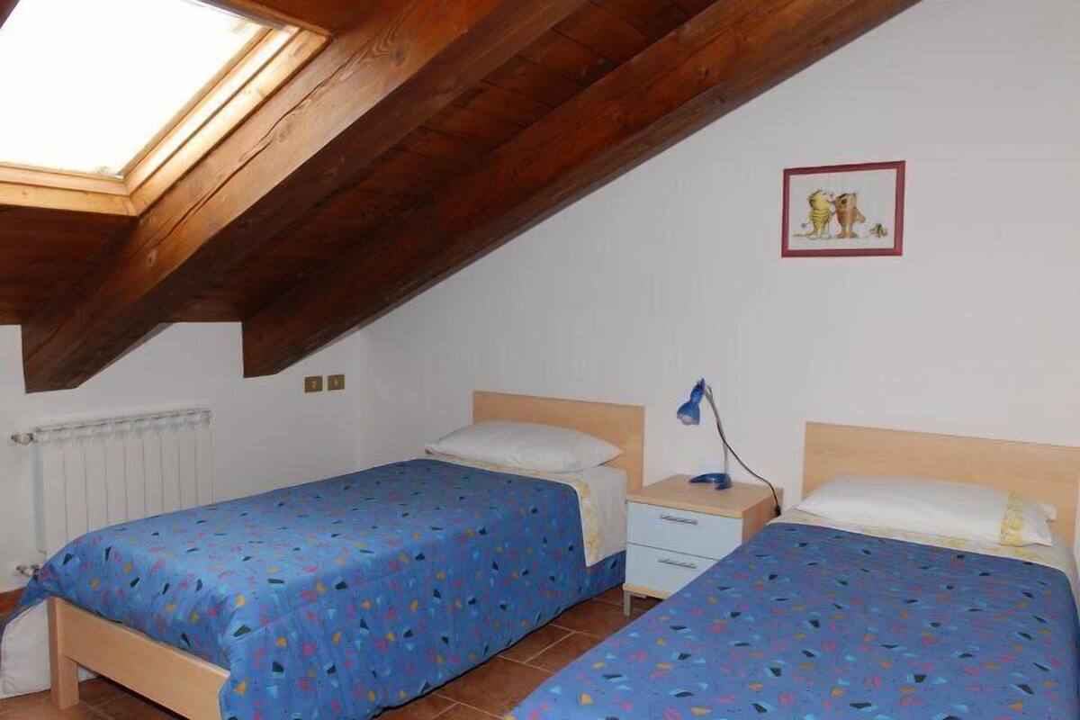 Quarto com duas camas, claraboia, radiador e um quadro na parede.