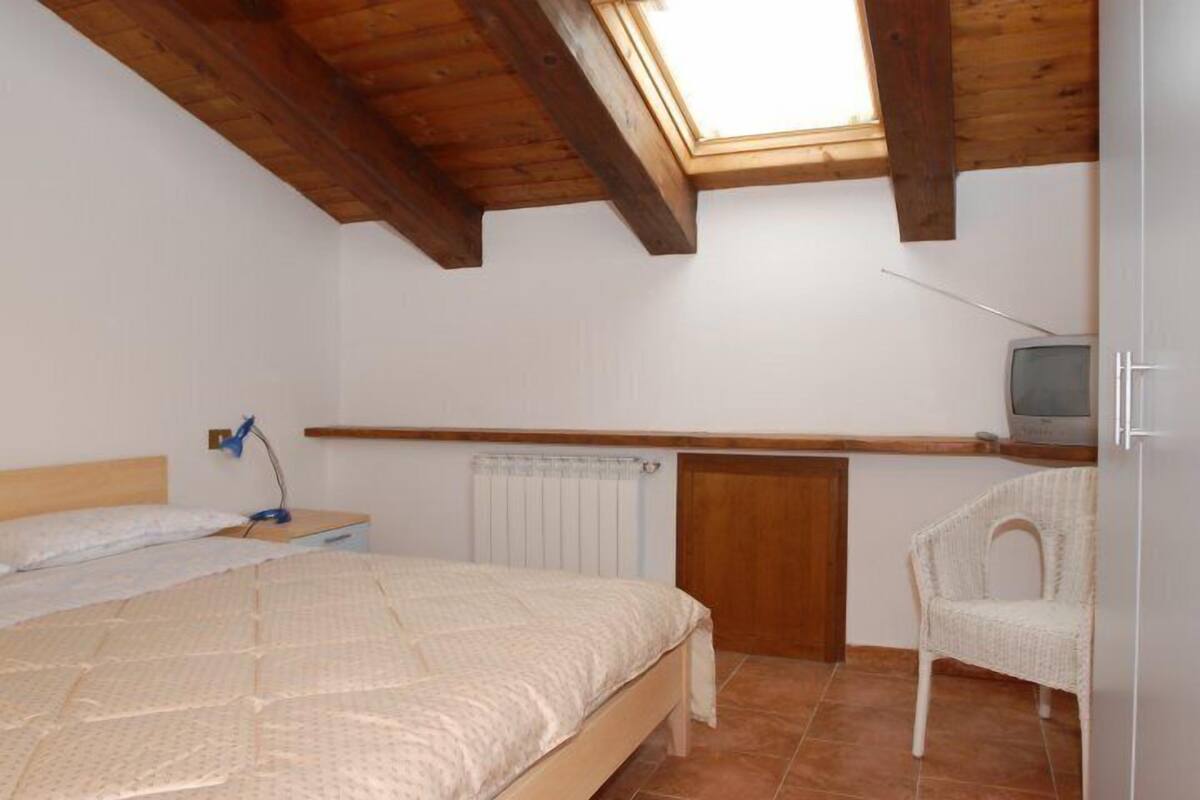 Quarto com cama, uma cadeira, televisão e um claraboia.