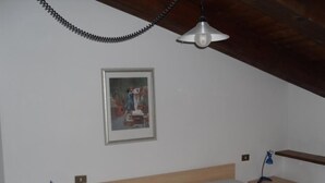 Et soveværelse med en træseng, et ternet tæppe, et skrivebord med en lampe og en hængende lampe.