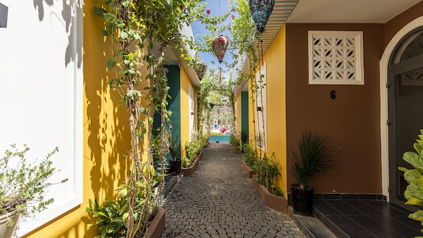 A narrow cobblestone alley flanked by yellow and brown buildings with potted plants and hanging lanterns. - O Dau Day Boutique Hotel (Ho Chi Minh City)