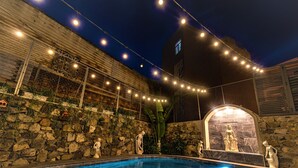 A swimming pool with stone walls and statues, string lights, and a stone archway. - O Dau Day Boutique Hotel (Ho Chi Minh City)