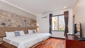 A bedroom with a stone wall, a bed with white bedding, a wooden floor, a desk with a telephone, and a window with curtains. - O Dau Day Boutique Hotel (Ho Chi Minh City)