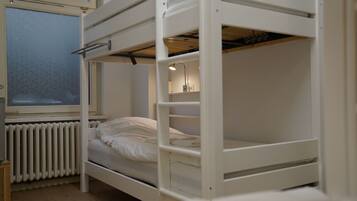 A bunk bed with a window, a radiator, and a shelf with items.