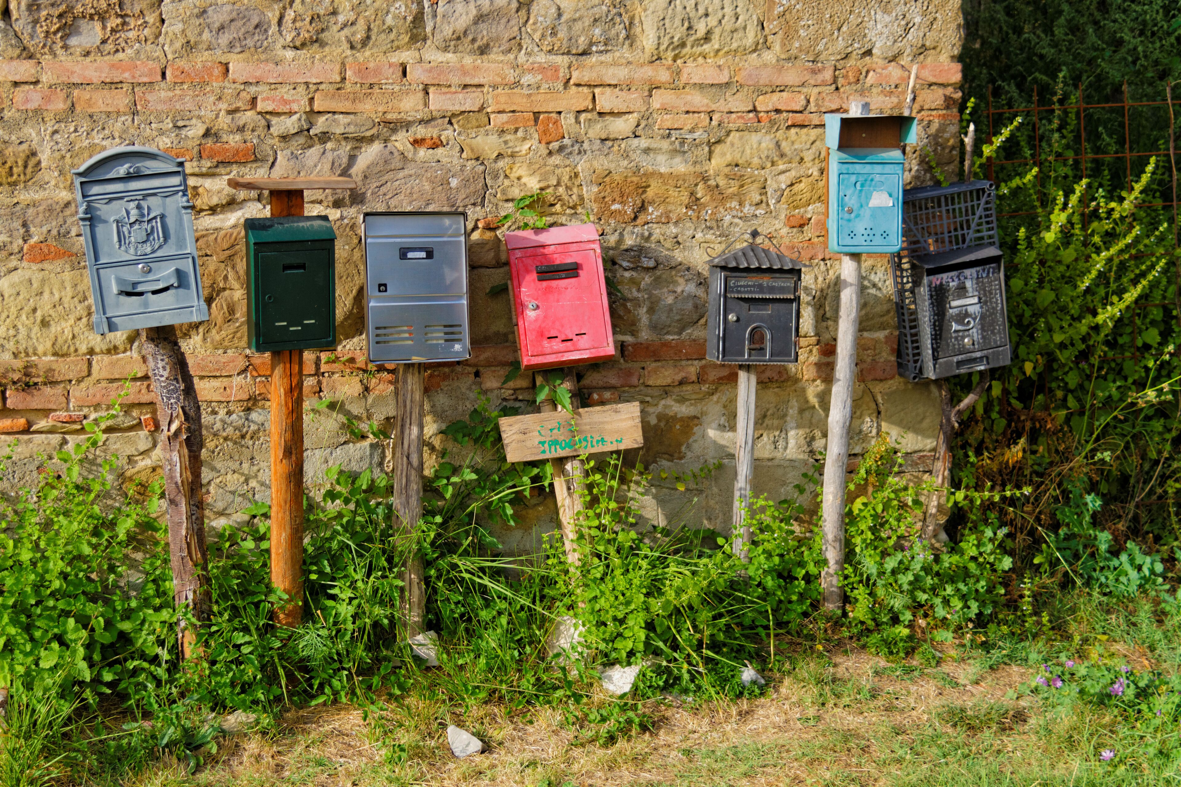 Una fila di cassette postali fissate a un muro di pietra, circondata dal verde.