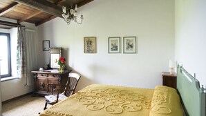Une chambre avec un plafond en bois, un lit recouvert d’une couverture jaune, une commode, une chaise et une fenêtre avec des rideaux.