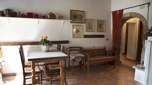 Un coin repas comprenant une table et des chaises en bois, un banc et une étagère où sont rangés divers ustensiles de cuisine.